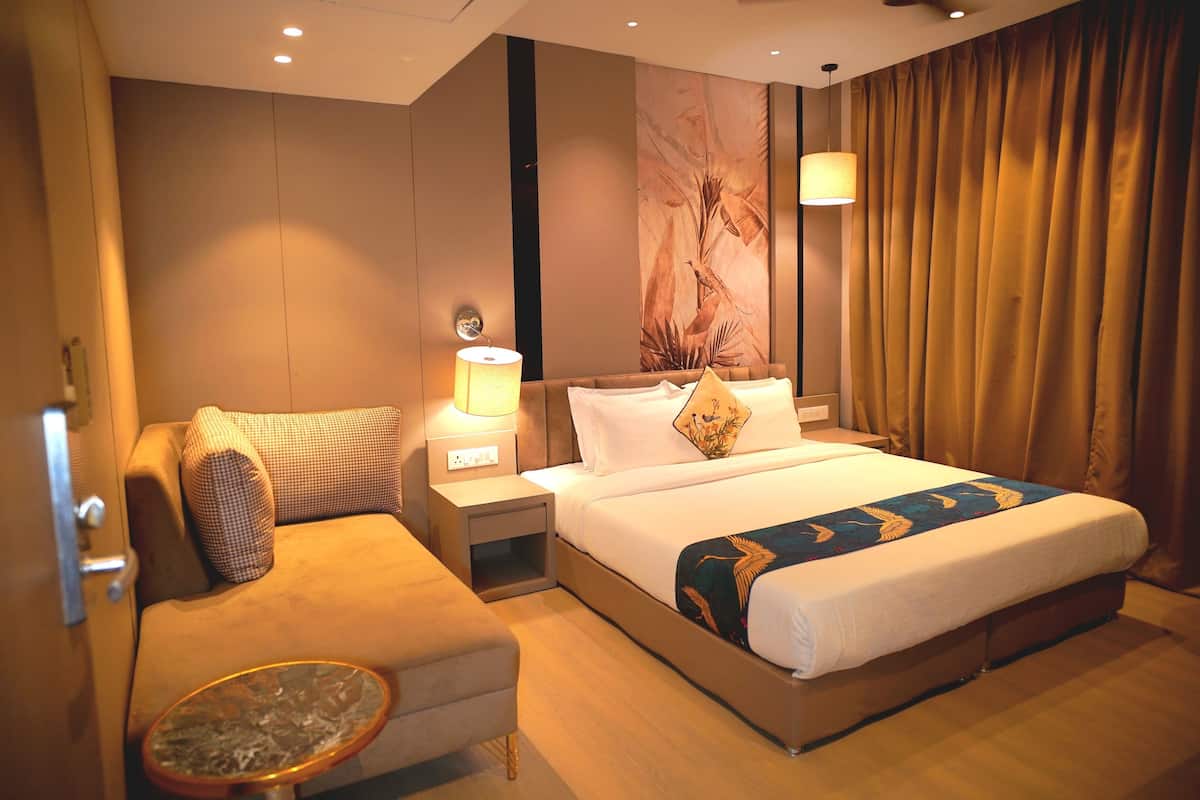 A hotel room with a bed, a sofa, a nightstand with a lamp, and a wall with a mural.
