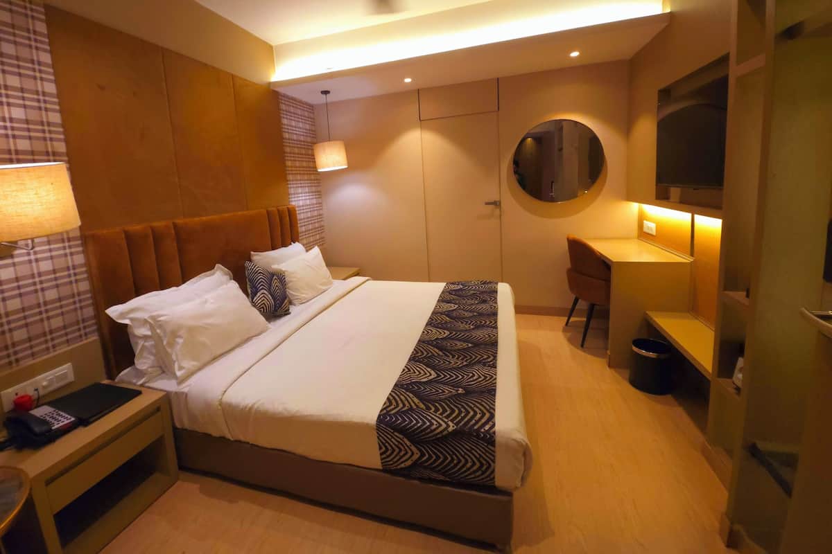 A hotel room with a bed, bedside table, lamp, desk, chair, and a mirror.