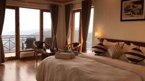 Ein Hotelzimmer mit einem großen Bett, einem Schreibtisch mit Stuhl und Blick auf die Berge durch die Fenster.