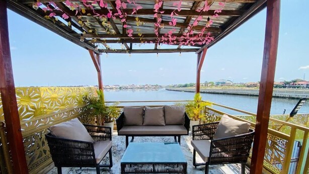 A covered outdoor seating area with a sofa and chairs, a table, and a view of a body of water. - Lakefront 2-BR-Apt With 24Hrs Power + Starlink Wi-Fi (Lagos)