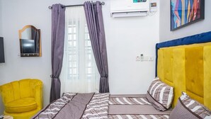 A bedroom with a bed, a yellow armchair, a mirror, and an air conditioning unit. - Lakefront 2-BR-Apt With 24Hrs Power + Starlink Wi-Fi (Lagos)