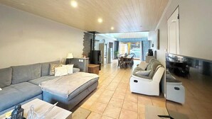 A spacious living area with a large grey sectional sofa, a white armchair, and a small table with a lamp. A television is mounted on the wall, and there is a door leading to another room. - Atypical enitre house with character, large volumes, tastefully decorated (Bourdons-sur-Rognon)