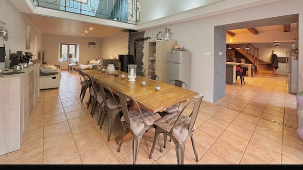 A spacious kitchen with a long dining table, a staircase leading to an upper level, and a view of the outdoors. - Atypical enitre house with character, large volumes, tastefully decorated (Bourdons-sur-Rognon)