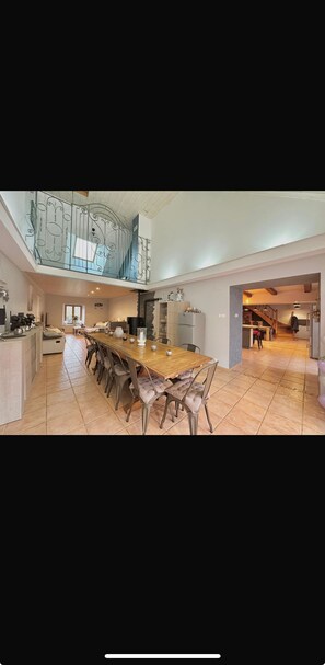 Une cuisine spacieuse avec une longue table à manger, un escalier menant à l’étage supérieur et une vue sur l’extérieur.