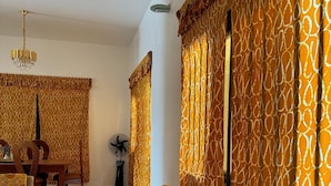 Un saló amb un sofà estampat, una zona de menjador amb taula i cadires, i un ventilador.