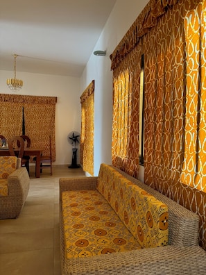 A living room with a patterned sofa, a dining area with a table and chairs, and a fan. - White House Rooftop (Ouidah)