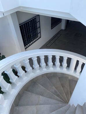 A spiral staircase with white balustrades and grey steps. - White House Rooftop (Ouidah)