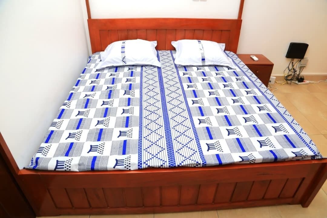 A single bed with a patterned bedspread, a wooden headboard, and a nightstand with a lamp.