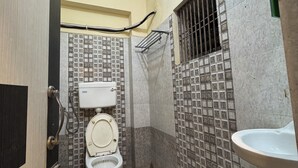 A small bathroom with a toilet, a sink, and tiled walls. - Hotel Asha Pride (Chatrapur)