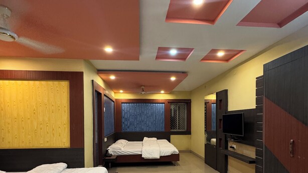 A hotel room with two beds, a TV, and a ceiling with recessed lighting. - Hotel Asha Pride (Chatrapur)