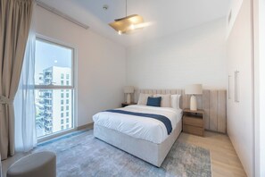 A hotel room with a large bed, bedside tables, a window with a view of buildings, and a ceiling light. - Bloomfields 1BR in Water's Edge 8- Yas (Abu Dhabi)
