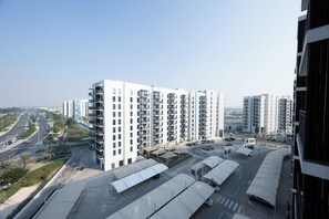 A high-rise residential building with multiple balconies, a parking area, and a clear view of the surrounding urban landscape. - Bloomfields 1BR in Water's Edge 8- Yas (Abu Dhabi)