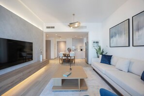 A modern living room with a flat-screen TV, a wooden coffee table, a sofa, and a dining area with chairs. - Bloomfields 1BR in Water's Edge 8- Yas (Abu Dhabi)