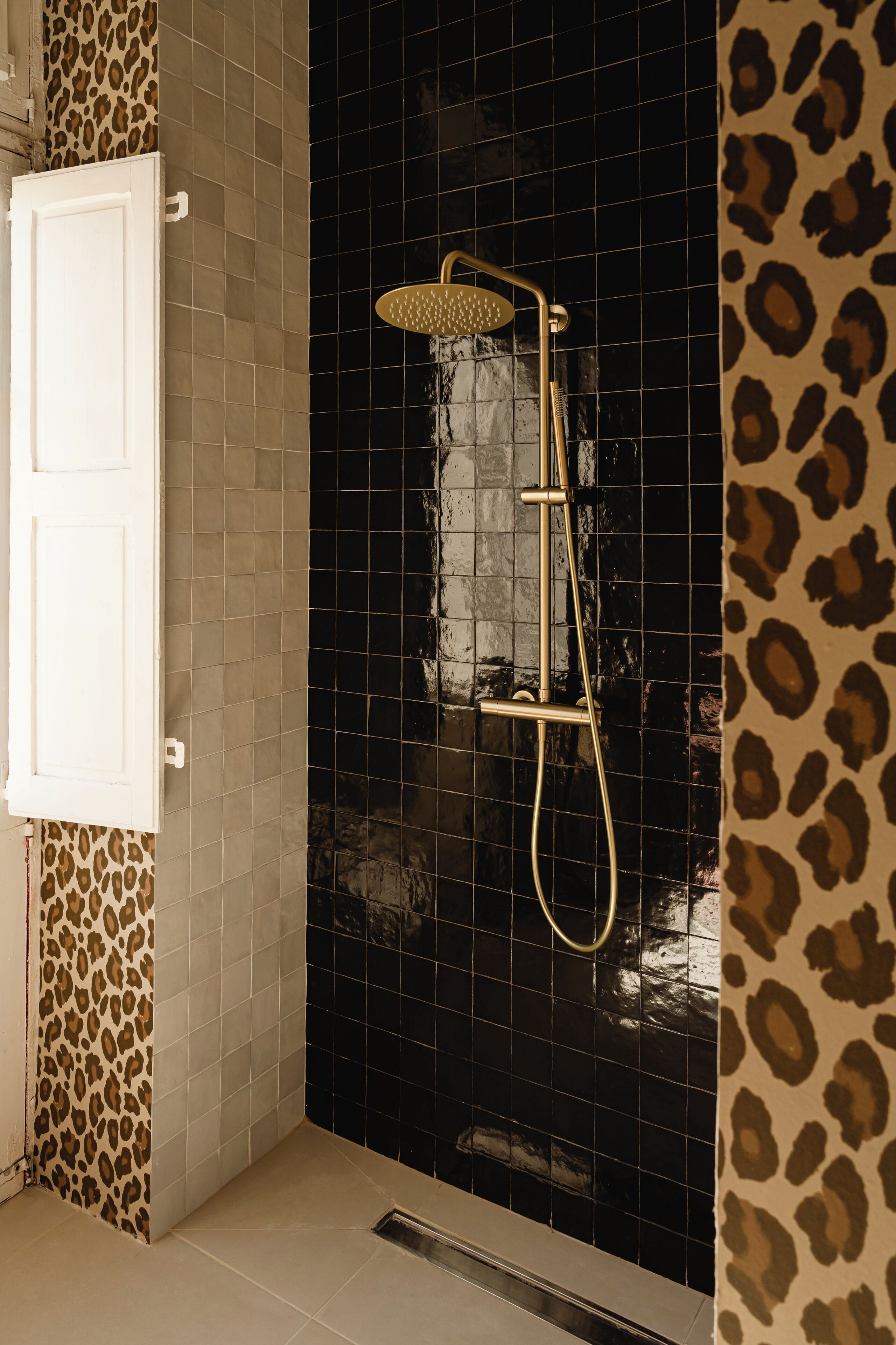 Een douche met gouden afwerking, een witte deur en een betegelde muur met luipaardprint.