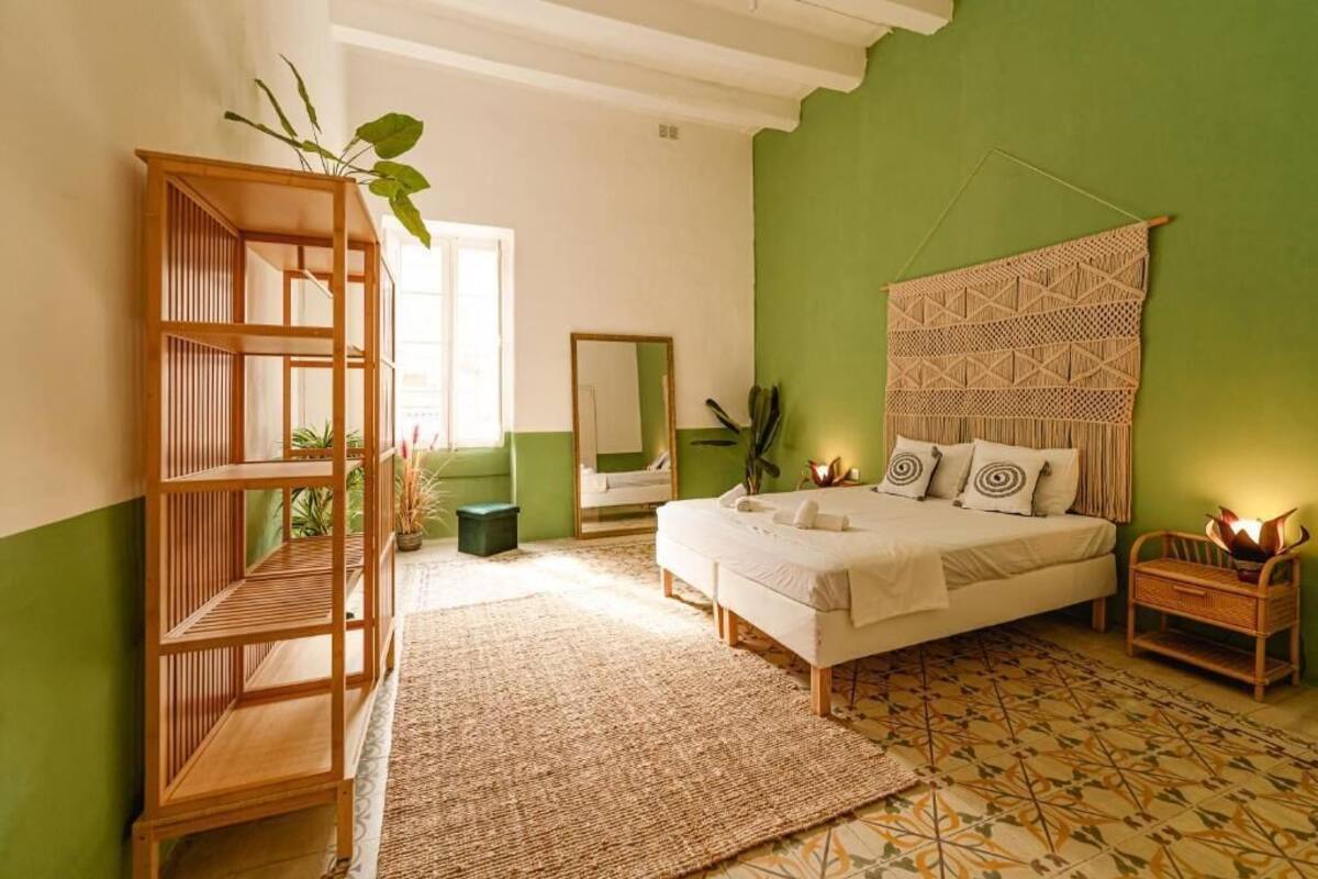 A bedroom with a bed, a wooden shelf, a mirror, and a wall hanging.