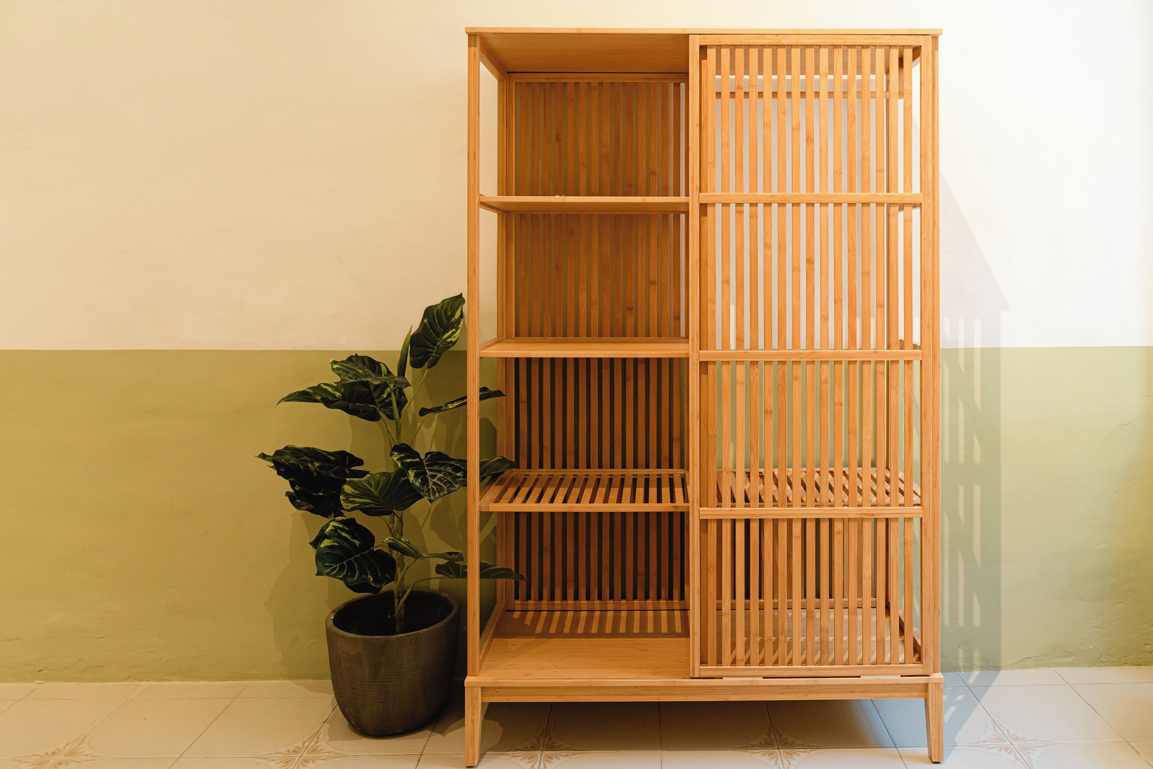 Una estantería de madera con varios estantes y una planta en maceta a su lado.