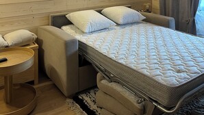A cozy bedroom with a wooden headboard, a bed with a quilted mattress, a small bedside table, and a chair. There are two framed pictures on the wall. - Le corbier Fully renovated 4-5 person apartment, at the foot of the slopes, view. (Villarembert)