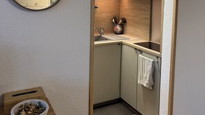 A compact kitchen with wooden cabinets, a sink, and a mirror. A clock is mounted on the wall, and a framed picture hangs above the mirror. - Le corbier Fully renovated 4-5 person apartment, at the foot of the slopes, view. (Villarembert)