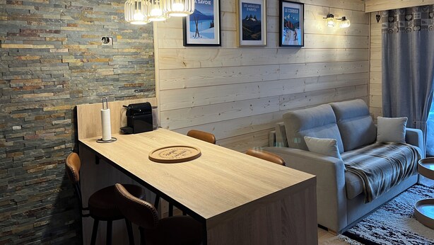 A modern living room with a wooden dining table, leather chairs, a grey sofa, and a stone wall. - Le corbier Fully renovated 4-5 person apartment, at the foot of the slopes, view. (Villarembert)