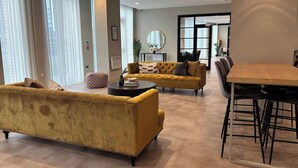Een moderne woonkamer met een gele bank, een ronde salontafel, en een eethoek met een houten tafel en stoelen.