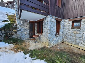 Ein Steinhaus mit Holzbalkon, einer kleinen Sitzgelegenheit im Freien und einem Fenster mit Blick auf die Berge.