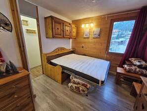 Una habitación acogedora con una cama de madera, una mesita de noche pequeña, un armario de madera y una ventana con vistas a un paisaje nevado.