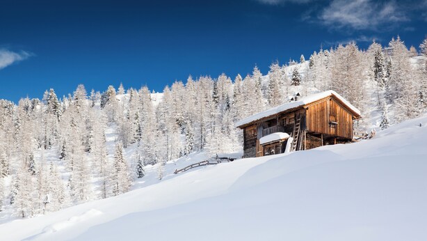 Eine Holzhütte auf einem verschneiten Berg unter blauem Himmel.