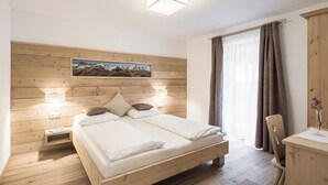 Ein Schlafzimmer mit einem hölzernen Kopfteil, einem Bett mit weißen Leinen, zwei Nachttischlampen, einem Nachttisch und einem Schreibtisch mit Stuhl.