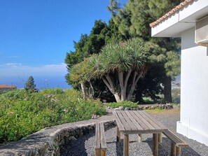 A patio area with a wooden table and benches, surrounded by a stone wall and various plants. - A cozy vacation home with a hot tub and a magnificent view of the Atlantic Ocean. (El Paso)