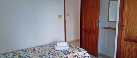 Un dormitori amb un llit, una tauleta de nit i un armari de fusta.