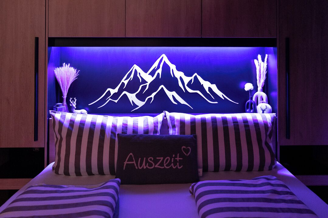 A bed with striped bedding and a pillow with the word "Auszeit" and a heart.