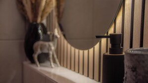 Een badkamer met een modern design, met een houten wandpaneel, een marmeren aanrecht en een zwarte zeepdispenser.