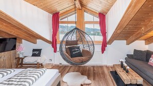 Een gezellige kamer met een hangstoel, een bed, een bank en een houten bijzettafeltje.