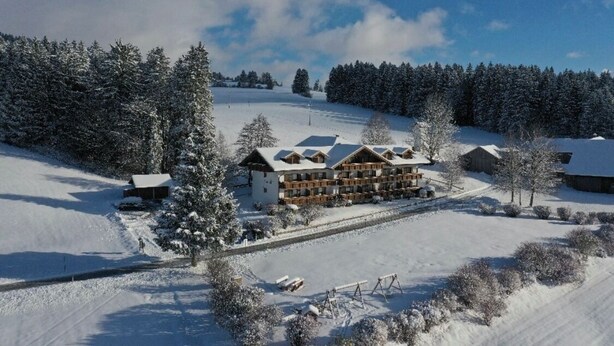 Een besneeuwd hotel met meerdere gebouwen, een piste en een bebost gebied.