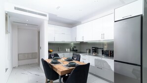 Une cuisine moderne avec des meubles blancs, un réfrigérateur en acier inoxydable et un coin repas comprenant une table en bois et des chaises noires.