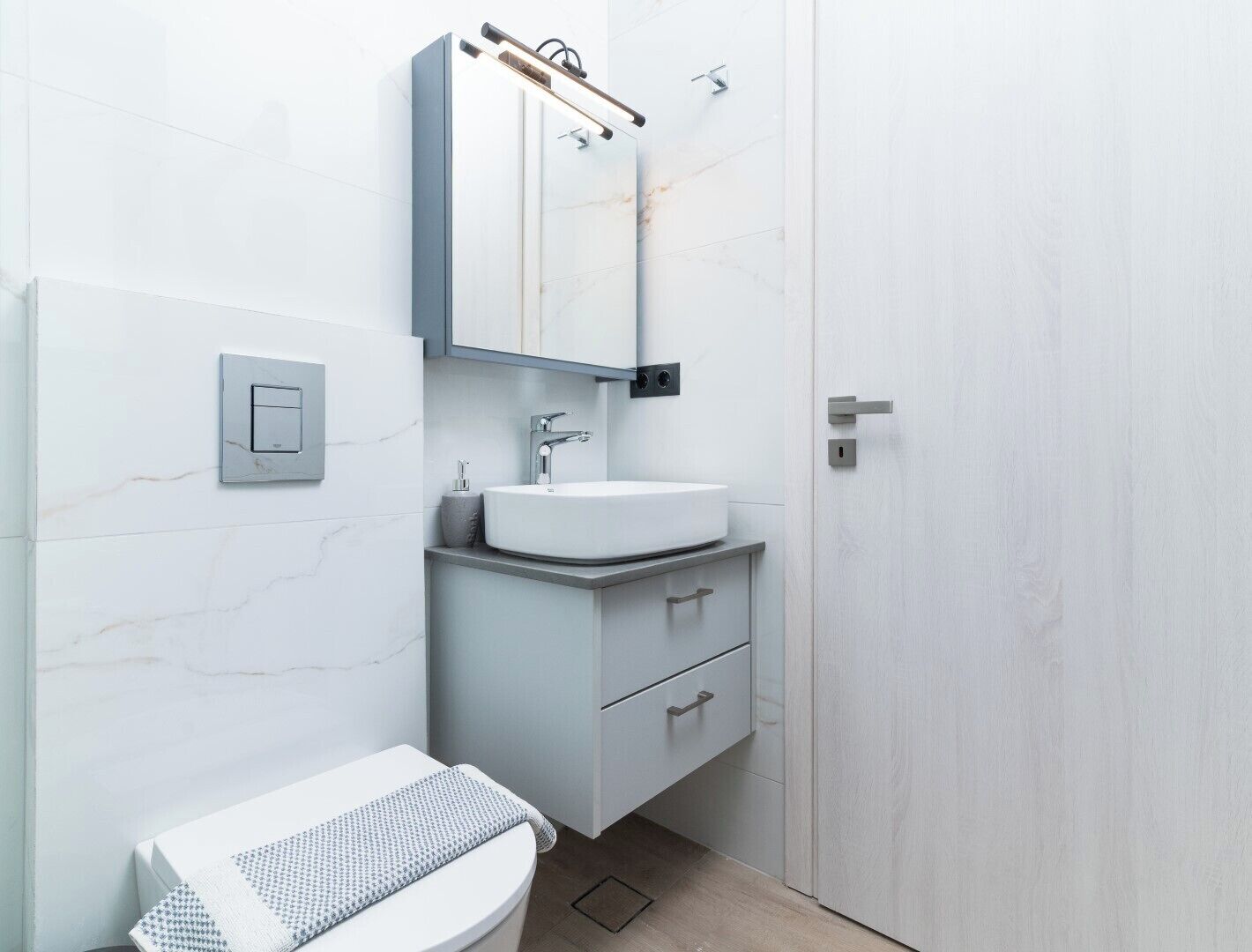 A modern bathroom with a white sink, a mirror, and a toilet.