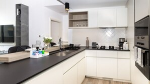 Una cocina moderna con armarios blancos, encimera negra y horno integrado. Hay un fregadero, un tostador y una cafetera en la encimera.