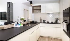 A modern kitchen with white cabinetry, a black countertop, and a built-in oven. There is a sink, a toaster, and a coffee maker on the counter. - Central Location with Easy Access to Al Khail Road, Near Bus Stops, Supermarkets, Dining Spots (Dubai)