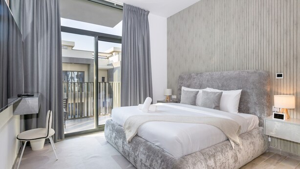 Un dormitorio moderno con una cama grande, una silla, vistas al balcón y una pared de madera.