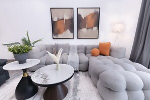 A modern living room with a grey sectional sofa, two round tables with black and gold bases, a potted plant, and abstract art on the wall. - Central Location with Easy Access to Al Khail Road, Near Bus Stops, Supermarkets, Dining Spots (Dubai)