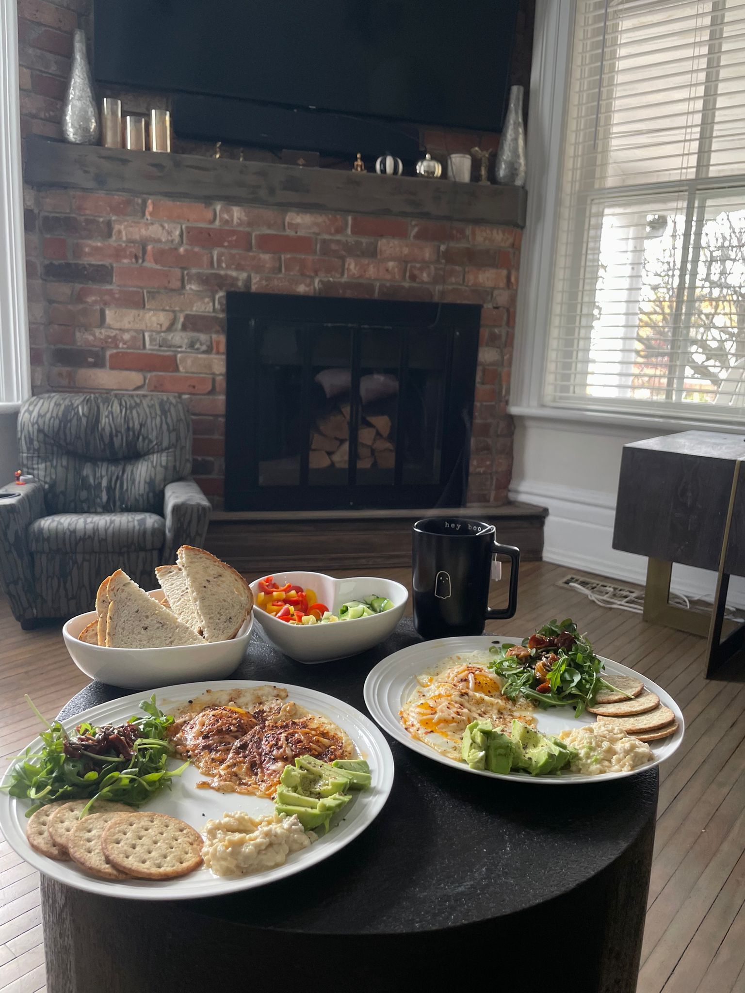 A dining area with a brick fireplace, a comfortable armchair, and a table set with plates of food.