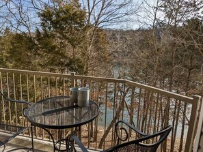 A balcony with a round metal table and chairs, overlooking a body of water and trees.