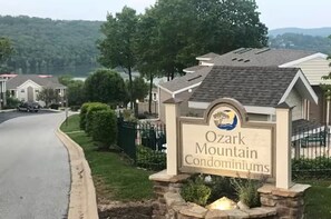 A sign for Ozark Mountain Condominiums with a view of a residential street and houses.