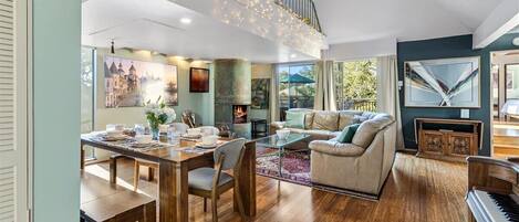 A spacious living area with a dining table, sofas, a piano, and a fireplace.