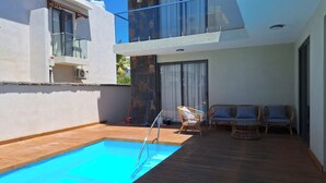 A modern outdoor pool area with a wooden deck, two wicker chairs, and a glass balustrade. - Amazing 4-bedroom villa in Grand Baie perfect for your getaway (Grand Baie)