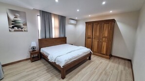A bedroom with a wooden bed, a nightstand, a wall-mounted air conditioner, and a large wardrobe. - Amazing 4-bedroom villa in Grand Baie perfect for your getaway (Grand Baie)