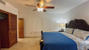 A bedroom with a bed, a ceiling fan, a nightstand, and a window. - Rainbow Rise: Oceanfront, Sunsets, Secluded beach, Backup Generator! (Cupecoy)