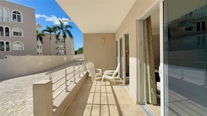 A balcony with two white chairs, a metal railing, and a view of palm trees and buildings. - Rainbow Rise: Oceanfront, Sunsets, Secluded beach, Backup Generator! (Cupecoy)