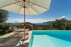 Una piscina con vistas claras al mar y a las colinas, una silla de descanso y una sombrilla.