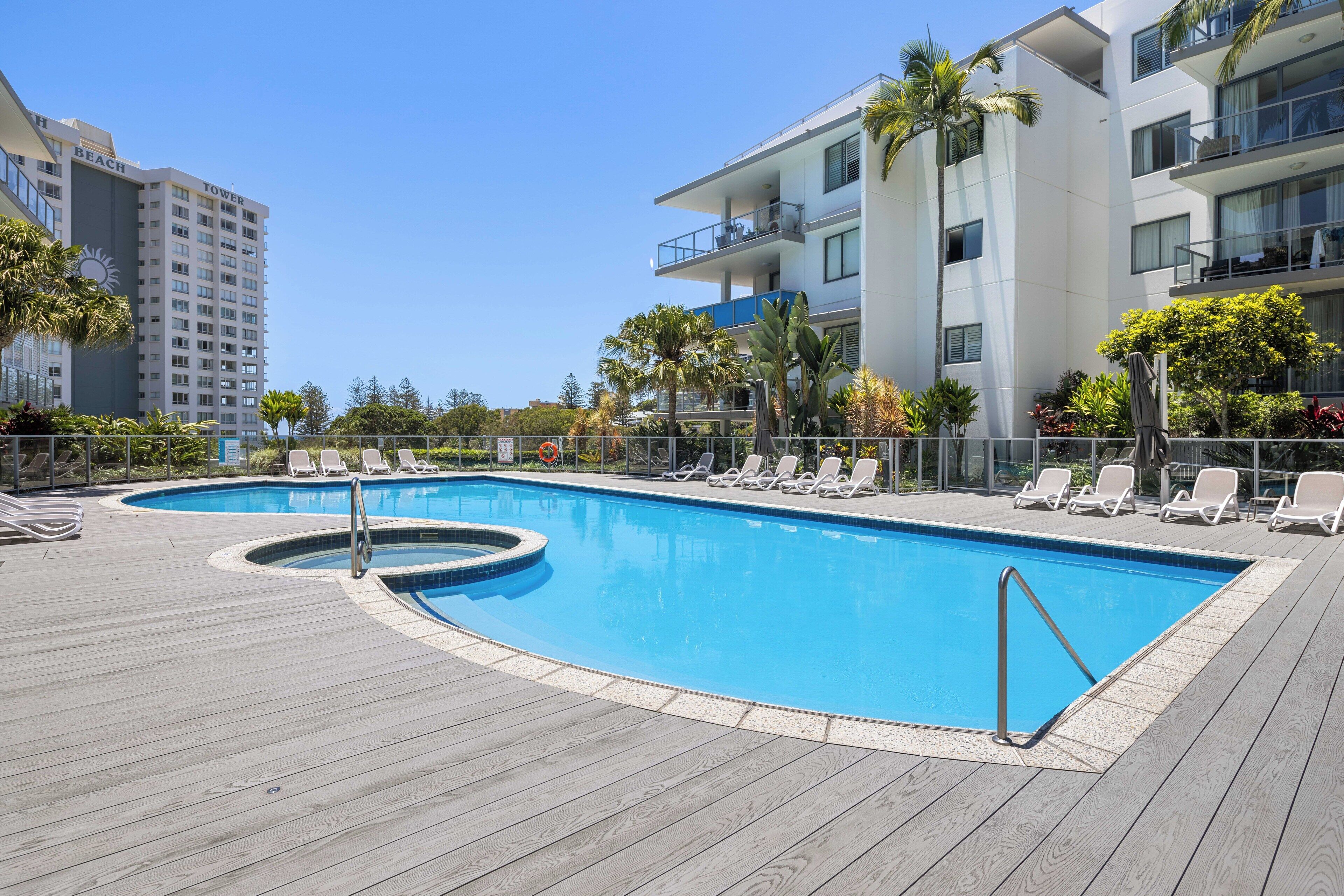 A swimming pool with lounge chairs, surrounded by a wooden deck and palm trees.